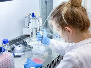 A female PhD student performing a biological experiment on a cancer cells in a sterile environment of designated biosafety laboratory at research facility. 