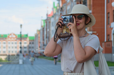 Blue color toned photo of beautiful woman tourist in a straw hat takes pictures on the street with a vintage camera