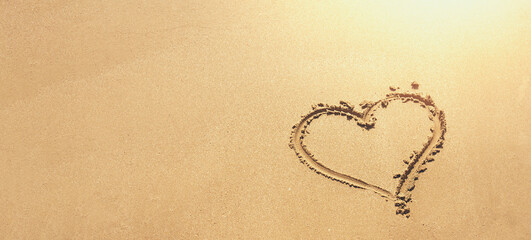 A heart shape drawn on smooth sand. Tropical beach banner background. Love sea and warm sunlight. Nature backdrop.