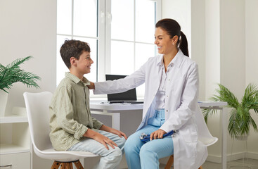 Teen boy at an appointment with a pediatrician in clinic. Professional woman doctor smiles and puts...