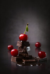 Pieces of dark chocolate and fresh cherry on a dark background. Copy space