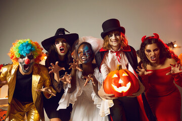 Group of young people dressed up as spooky characters having fun at Halloween costume party. Adult male and female friends with scary makeup on faces doing claw gesture, hissing and making grimaces - Powered by Adobe