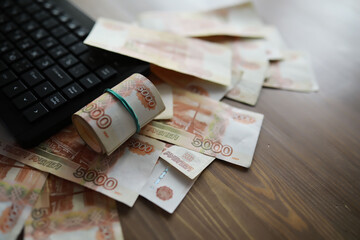 Stacks of 5000 ruble banknotes on the table next to the laptop. Savings and investments in the conditions of sanctions and inflation.