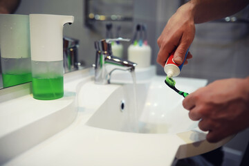 Hands with tooth brush and paste on blurred background in the bathroom in the sink. Selective focus.