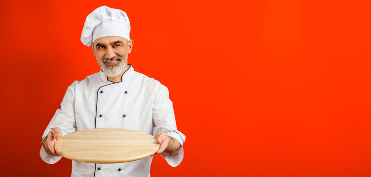 Chef-cooker in a chef's hat and jacket holding an empty wooden tray for mock up. Senior professional baker man wearing a chef's outfit. Character kitchener, pastry chef for advertising