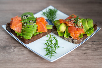 smoked salmon, avocado, dill, sesame seeds, arugula leaf green rocket on toast on white plate. Concept of healthy eating lifestyle diet nutrition. Omega 3 fatty acids source. Weight loss diet 