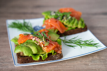 smoked salmon, avocado, dill, sesame seeds, arugula leaf green rocket on toast on white plate. Concept of healthy eating lifestyle diet nutrition. Omega 3 fatty acids source. Weight loss diet 
