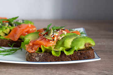 smoked salmon, avocado, dill, sesame seeds, arugula leaf green rocket on toast on white plate. Concept of healthy eating lifestyle diet nutrition. Omega 3 fatty acids source. Weight loss diet 
