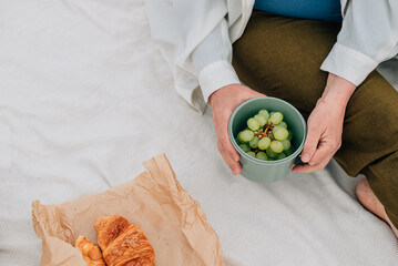 close-up. An adult woman holds grapes in her hands against the background of a plaid, croissants on...