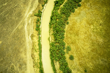 a winding muddy river with overgrown green banks in a sun-scorched steppe rural landscape