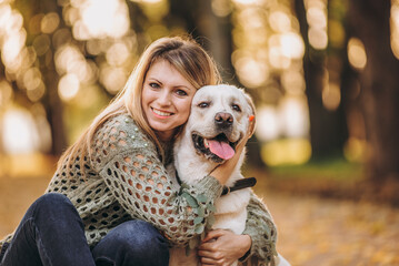 A young blonde woman is playing in the autumn park with her labrador. Evening walk with a labrador.