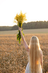 A girl with long hair holding a bouquet of flowers in the field. The concept of freedom, prosperity, fertility. Soft focus.