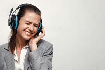 A girl in a gray jacket and a white shirt listens to music with pleasure, showing a funny grimace and thumbs up