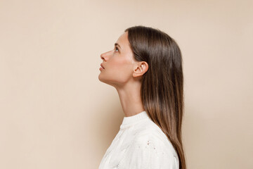 Caucasian female with long shiny hair with nude makeup in profile on a beige background - Powered by Adobe