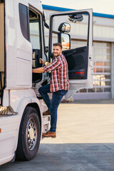 Photo of motivated smiling middle aged truck driver entering his semi truck long vehicle. Happy...