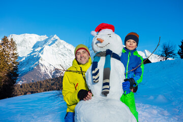 Family fun father and a boy build snowman with in scarf, carrot