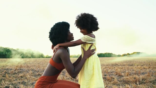 Cinematic video of an african girl with afro haircut and her daughter in a sunflowers field	