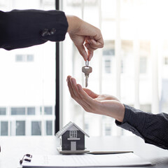 Sales manager or real estate agent holds the key handing it to the customer after signing the house purchase contract with home insurance, Trading of mortgages and insurance concept.