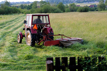 Old red tractor, cutting up hay in a field