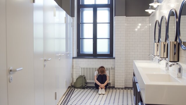 Sad and lonely teen girl sit on restroom floor alone
