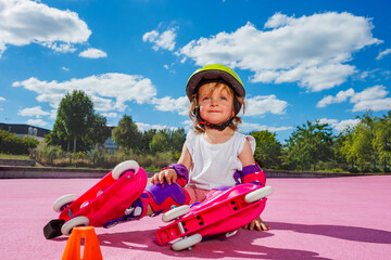 Girl learn rollers, sit in protection on color floor of the park