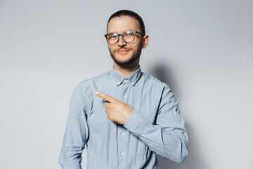 Studio portrait of young smiling man point finger away, wearing eyeglasses and blue t-shirt on white background.