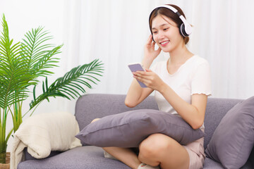 Obraz premium Lifestyle in living room concept, Young Asian woman in headphone to listening music on smartphone