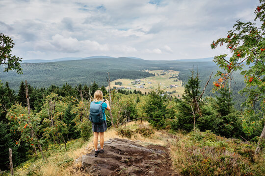 Female traveler use smartphone to take picture of Jizerka village,Bukovec,Czech Republic.Travel concept and technology.Tourist taking picture of nature.Woman photographer with backpack making photos