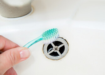 Close up view of woman hand cleaning bathroom sink with toothbrush. Home cleaning hack, fits small...