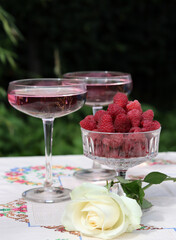 Romantic picnic in a garden. Rose wine, bowl with raspberry, white roses on a table. Summer outdoors photo. 