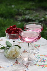 Romantic picnic in a garden. Rose wine, bowl with raspberry, white roses on a table. Summer outdoors photo. 