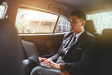 Young Asian businessman using a laptop in the backseat of a car.