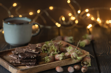 Pieces of chocolate with nuts, hazelnuts and a mug with cocoa on a dark background with bokeh.