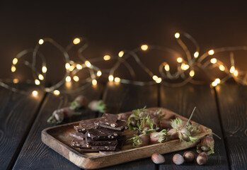 Pieces of chocolate with nuts, hazelnuts on a dark background with bokeh.
