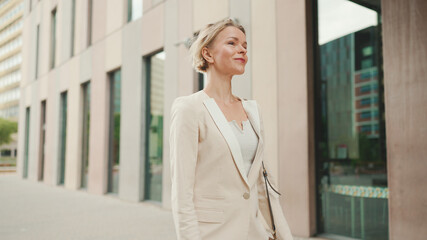 Businesswoman in beige suit walks outside past business building