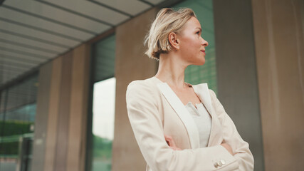 Smiling woman with blond hair wearing beige suit walks down the street and looks around