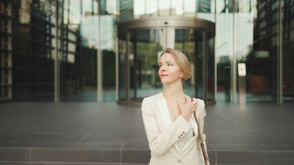 Businesswoman with blond hair wearing beige suit leaving business center - obrazy, fototapety, plakaty