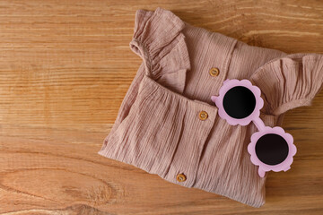 Stylish child clothes and sunglasses on wooden background, flat lay. Space for text
