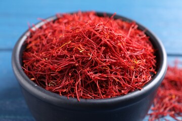 Dried saffron in bowl on blue table, closeup