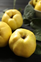 Fresh ripe organic quinces with leaves on black table, closeup
