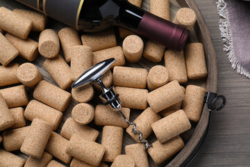 Corkscrew, wine bottle and stoppers on wooden tray, top view