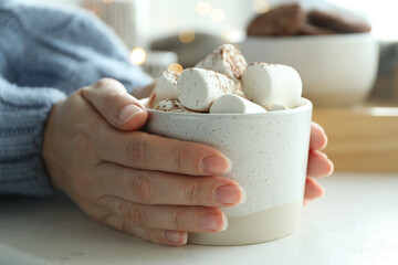Fototapeta na wymiar Woman holding cup of delicious hot cocoa with marshmallows at white table indoors, closeup. Winter drink