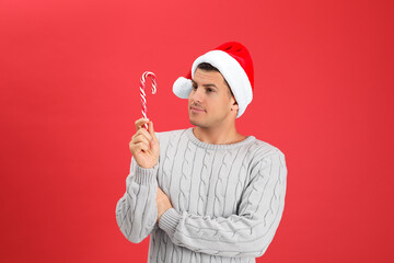 Handsome man in Santa hat holding candy cane on red background - Powered by Adobe
