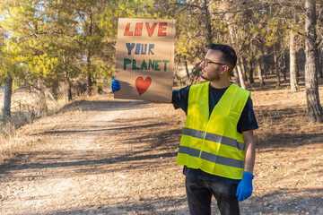 Hombre voluntario, con pancarta de ama tu planeta, en el bosque, en forma de protesta. Fotografía...