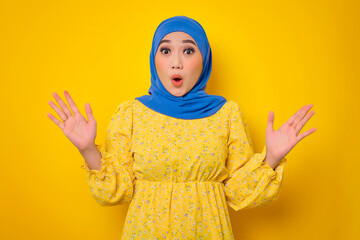 Shocked young Asian woman in casual dress looking at camera with opened mouth, spreading hands...