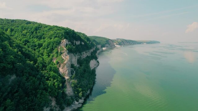 Shot on a drone. The border of water and land. The hilly shore of a wide river. Rocky steep coast. Beautiful landscape.
