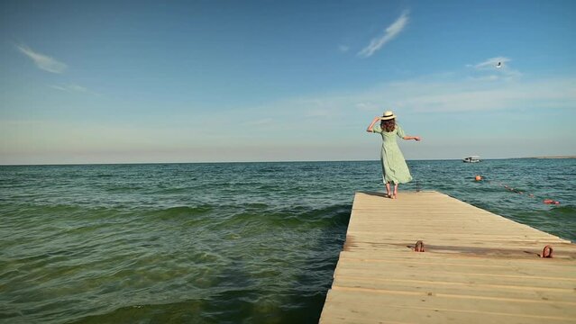Slow motion woman in a dress in the wind walks along the pier on the seashore on a sunny day