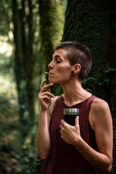 Woman smoking in forest holding camping mug
