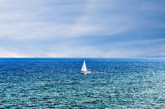 Scene Of A Small Boat With Sail In The Middle Of The Blue Ocean