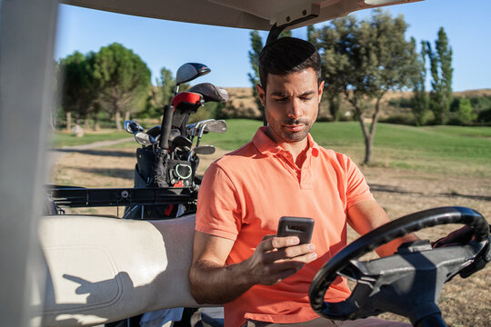Golfer chatting on smartphone in golf cart in countryside field - Powered by Adobe